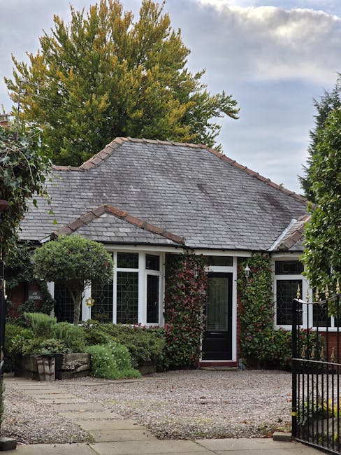 A small front garden in Colindale featuring a single-story house with a tiled sloping roof and white-framed bay windows. The garden includes a gravel pathway leading to the front door, which is partia